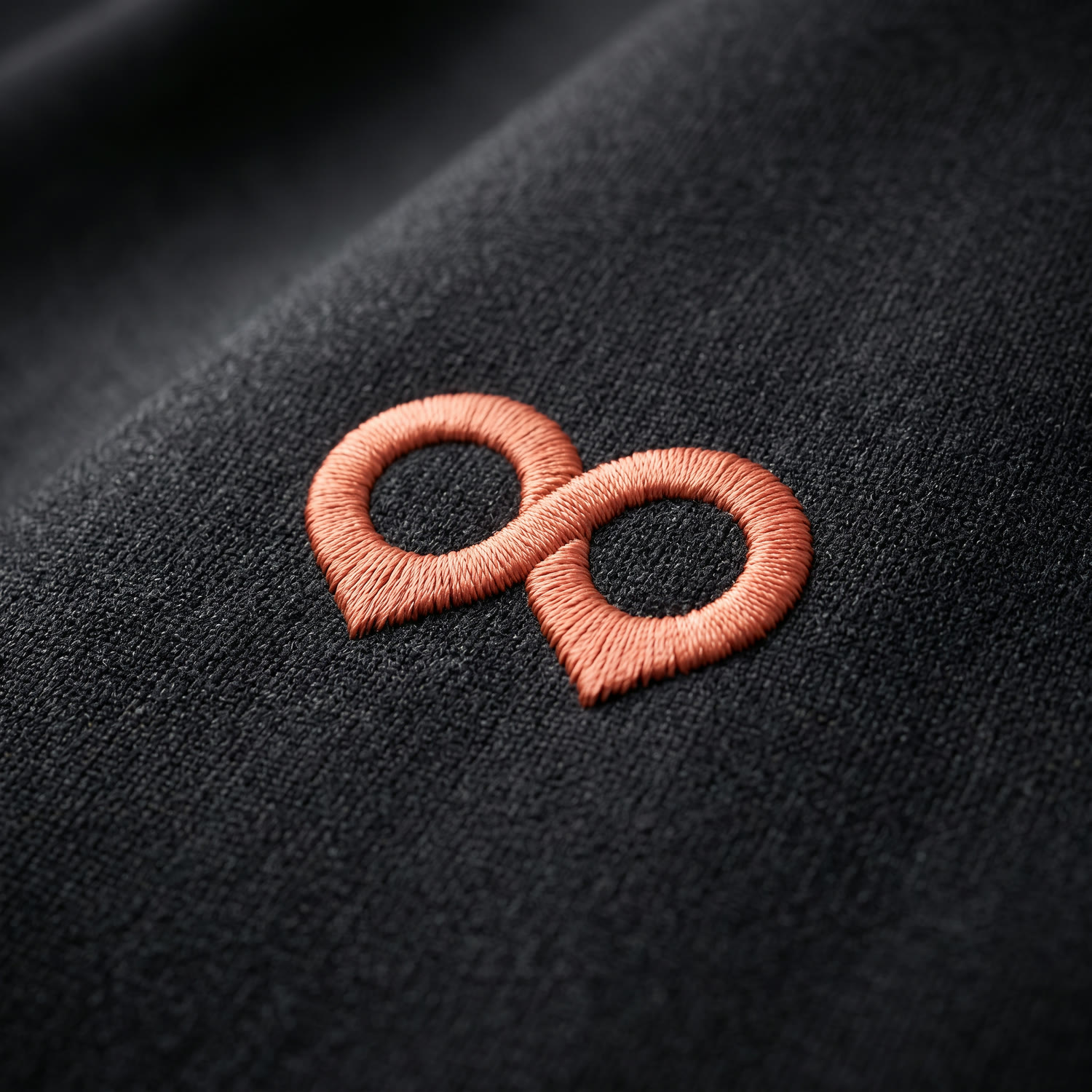 The mark embroidered in coral thread on dark woven fabric.
